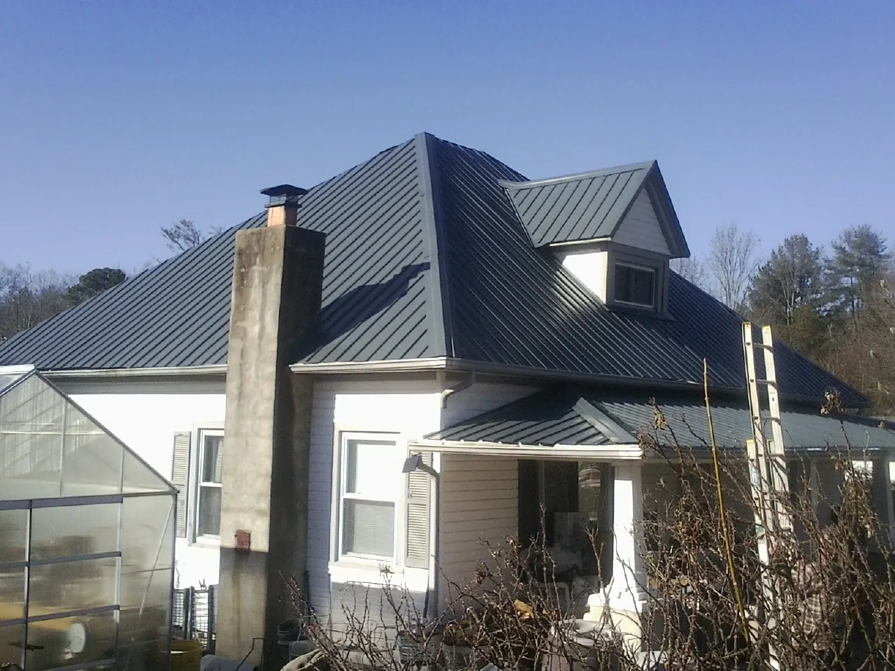 Dark blue standing seam metal roof on a white farmhouse with dormer — Slate & Tile Roof Repair by Roofing Brothers in New Roads