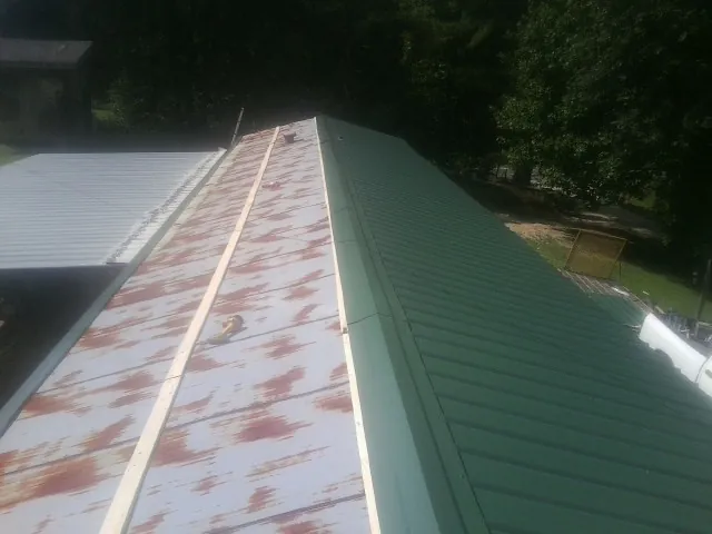 Old rusted panels beside newly installed green metal roofing — Wind Damage Roof Repair by Roofing Brothers in New Roads