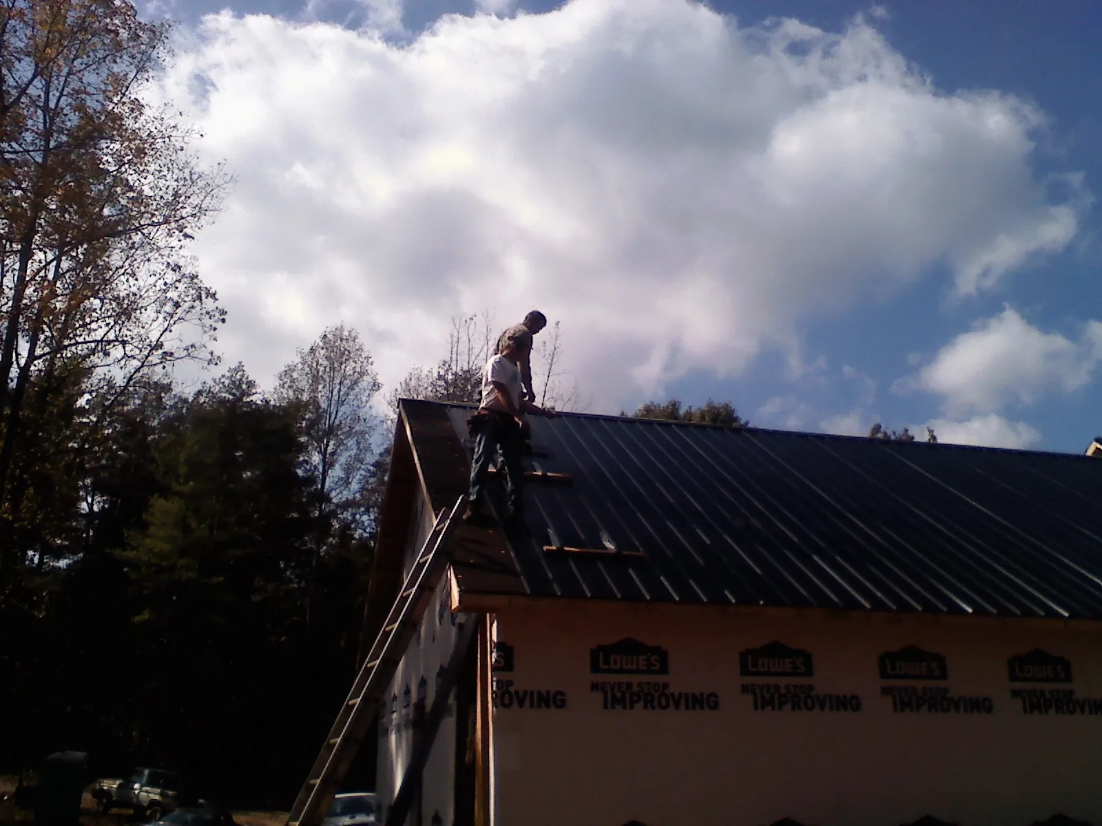 Roofer fastening dark metal panels high against a cloudy sky, from a Roof Inspection job in New Roads
