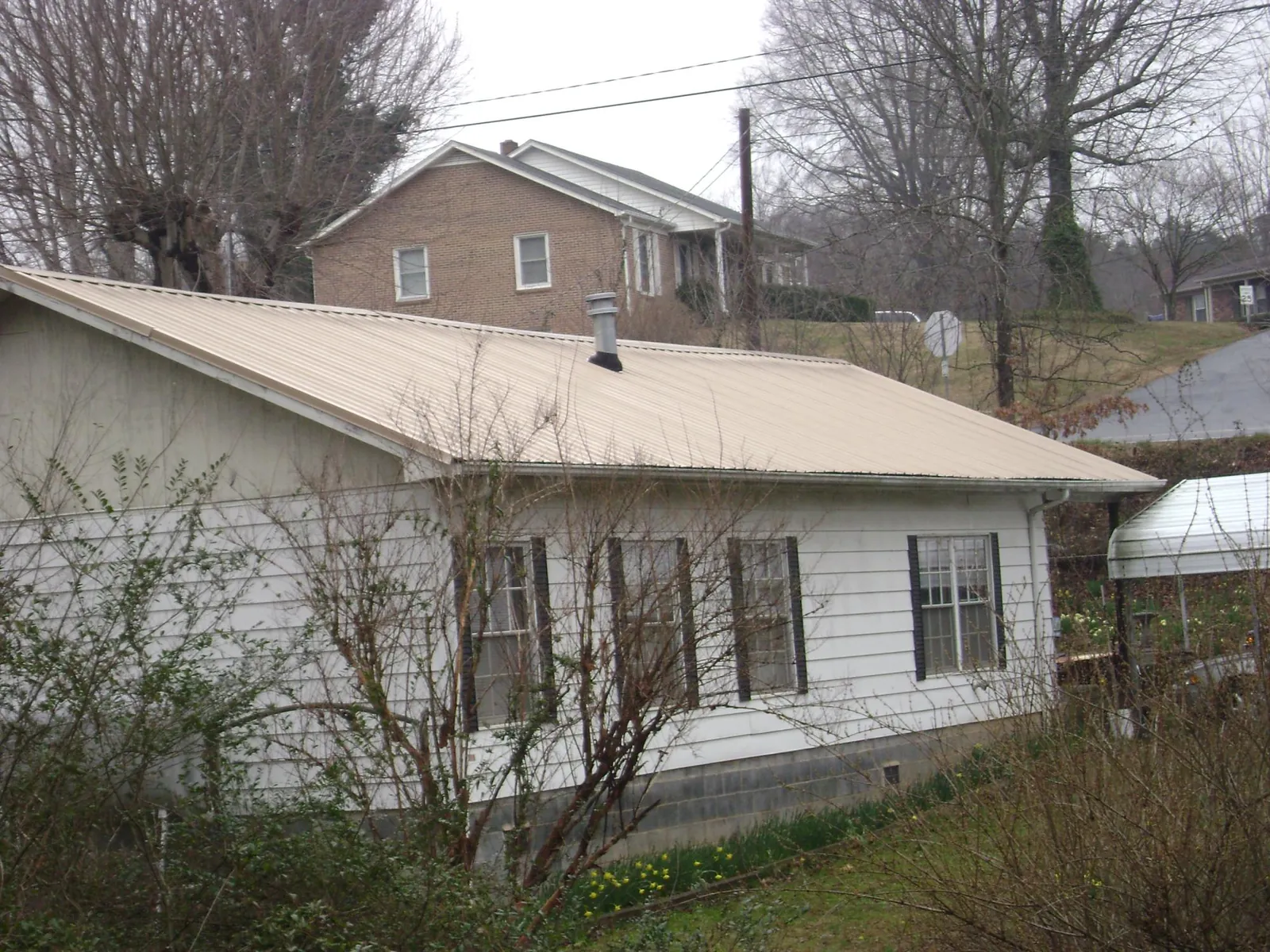 Tan metal roof on a white sided house set into a hillside — Commercial Roofing by Roofing Brothers in New Roads